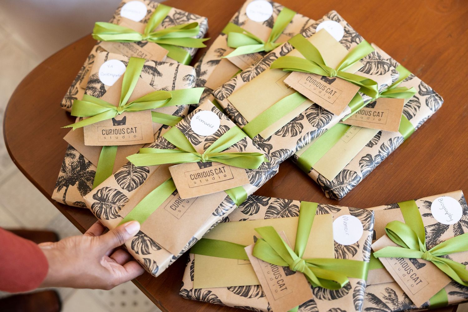 Wrapped gifts in botanical print paper tied with green ribbons displayed on a wooden table.