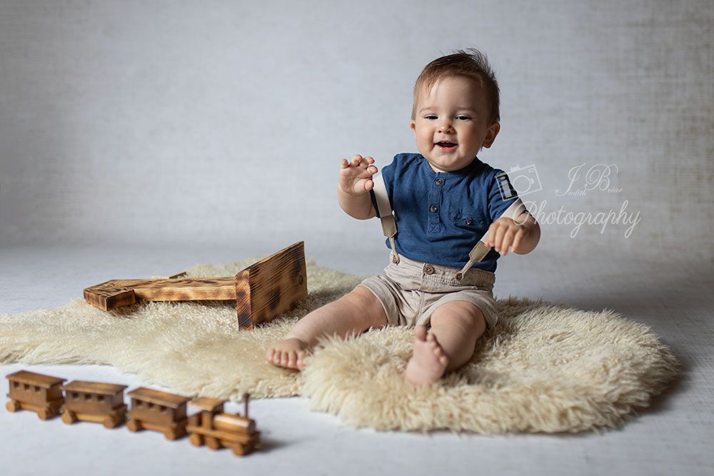 Geburtstagsfotografie. Junge sitzt auf einem Fell und freut sich über einen Holzzug. Babyfotos Gelsenkirchen, Herten