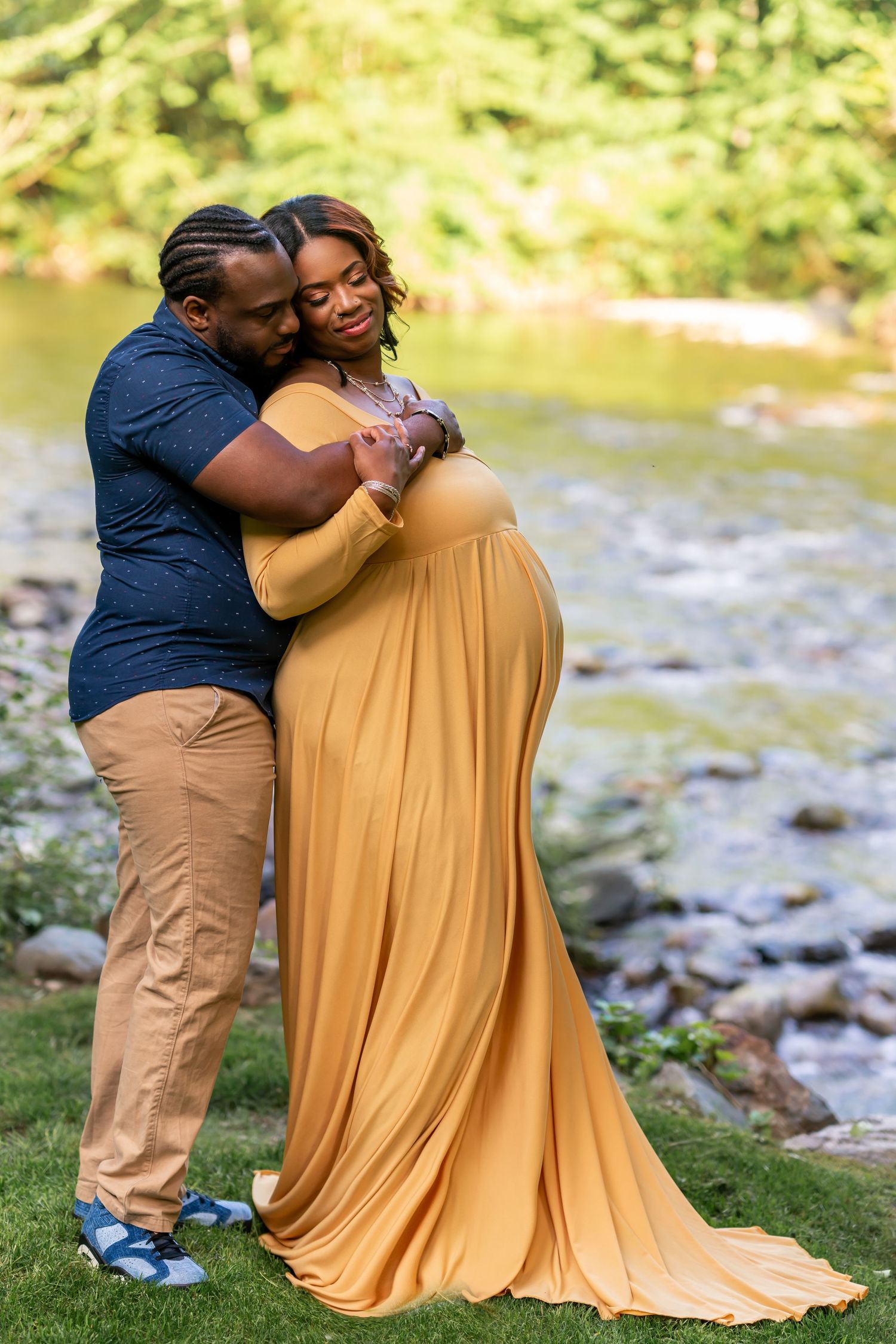 Romantic maternity photo of couple embracing by stream in golden dress and navy shirt.