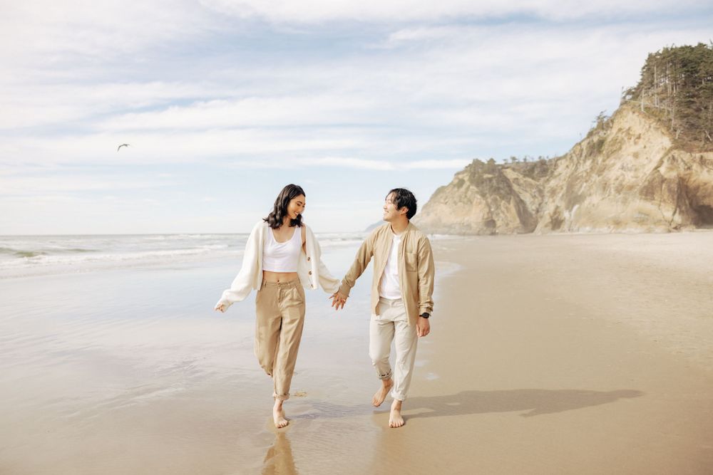 A couple walks hand in hand along a scenic beach with cliffs in the background.