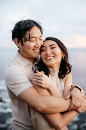 A joyful couple shares a tender moment while embracing on a coastal cliff.