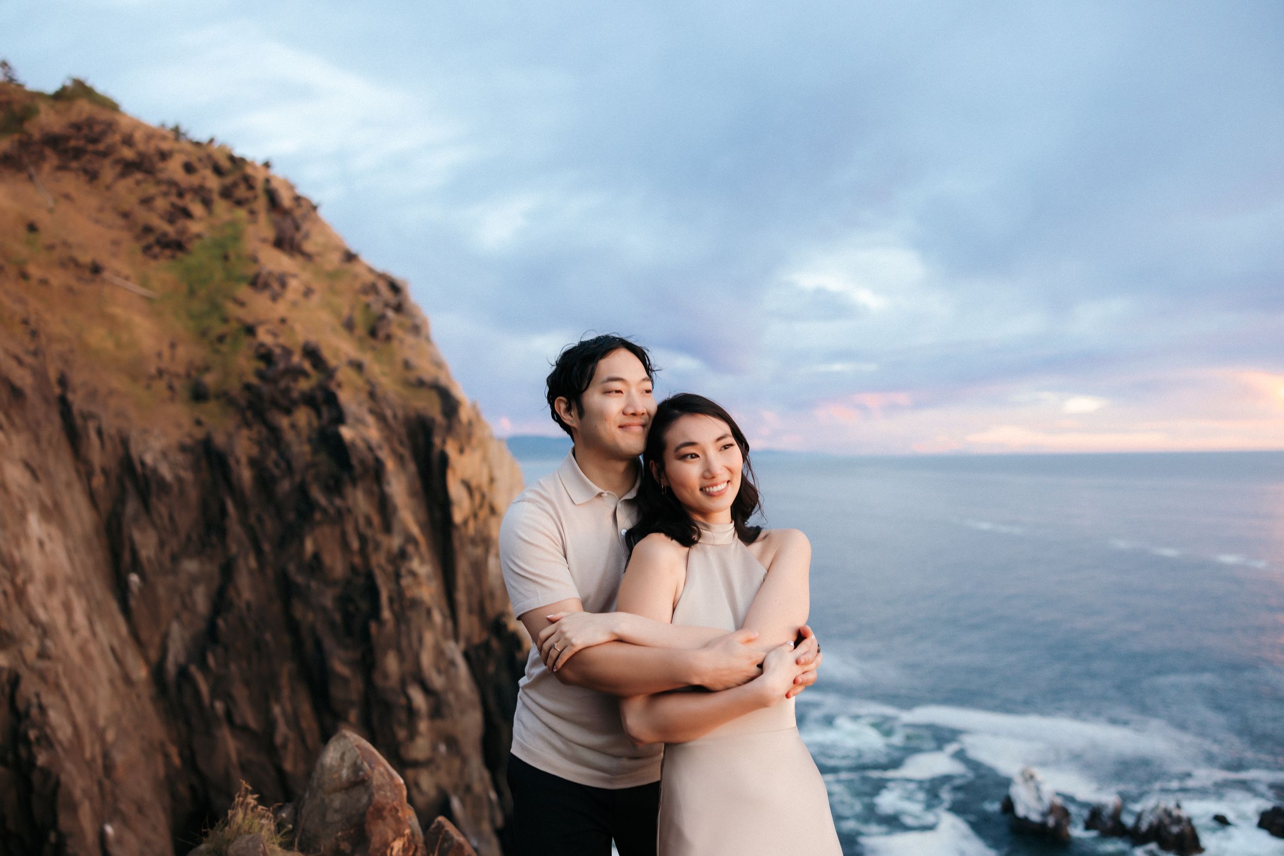 A couple embraces against dramatic coastal cliffs during sunset.