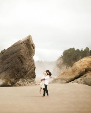 A couple shares a romantic moment on a misty beach surrounded by towering rock formations.
