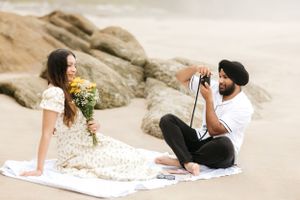 A couple has a beach picnic while taking photos against dramatic coastal cliffs.