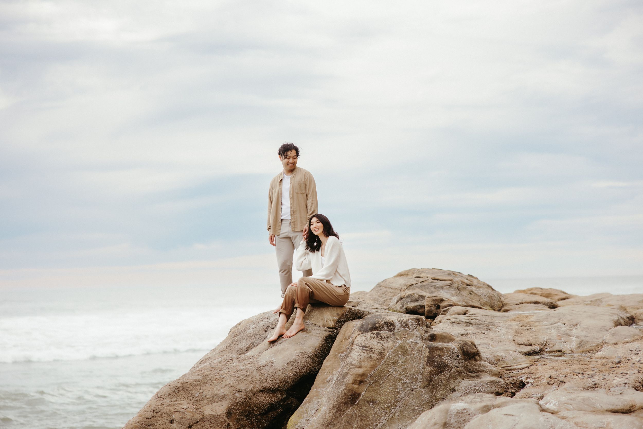 Two people share an intimate moment while sitting on coastal rocks overlooking the ocean.