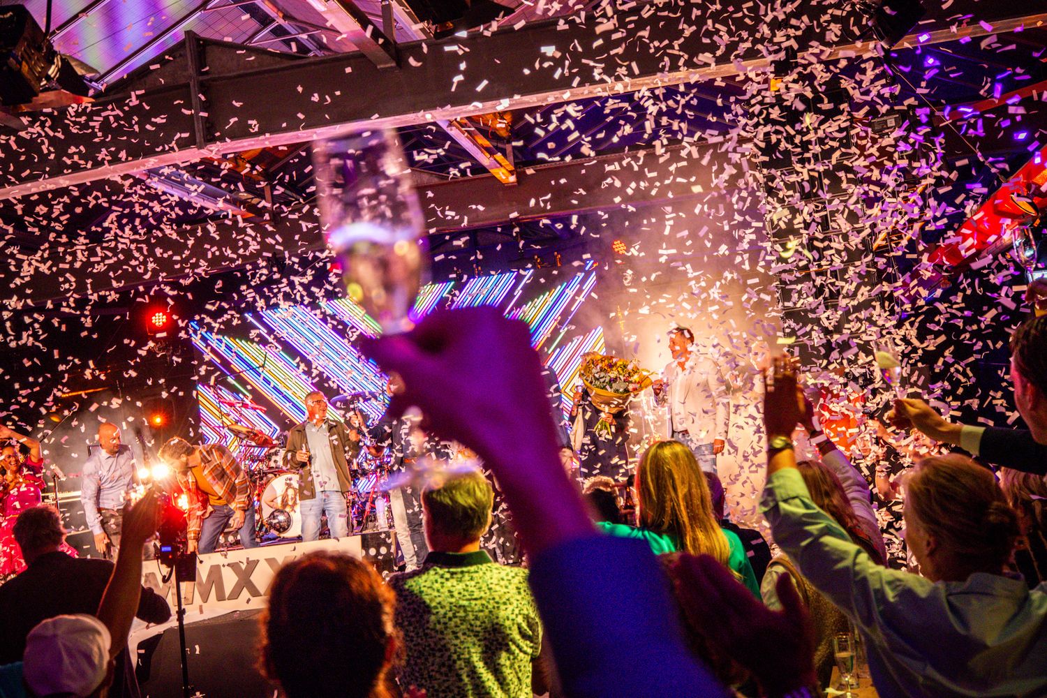 Feestelijke sfeer met champagneglas in de lucht, confetti in de lucht en handen in de lucht tijdens een feest.