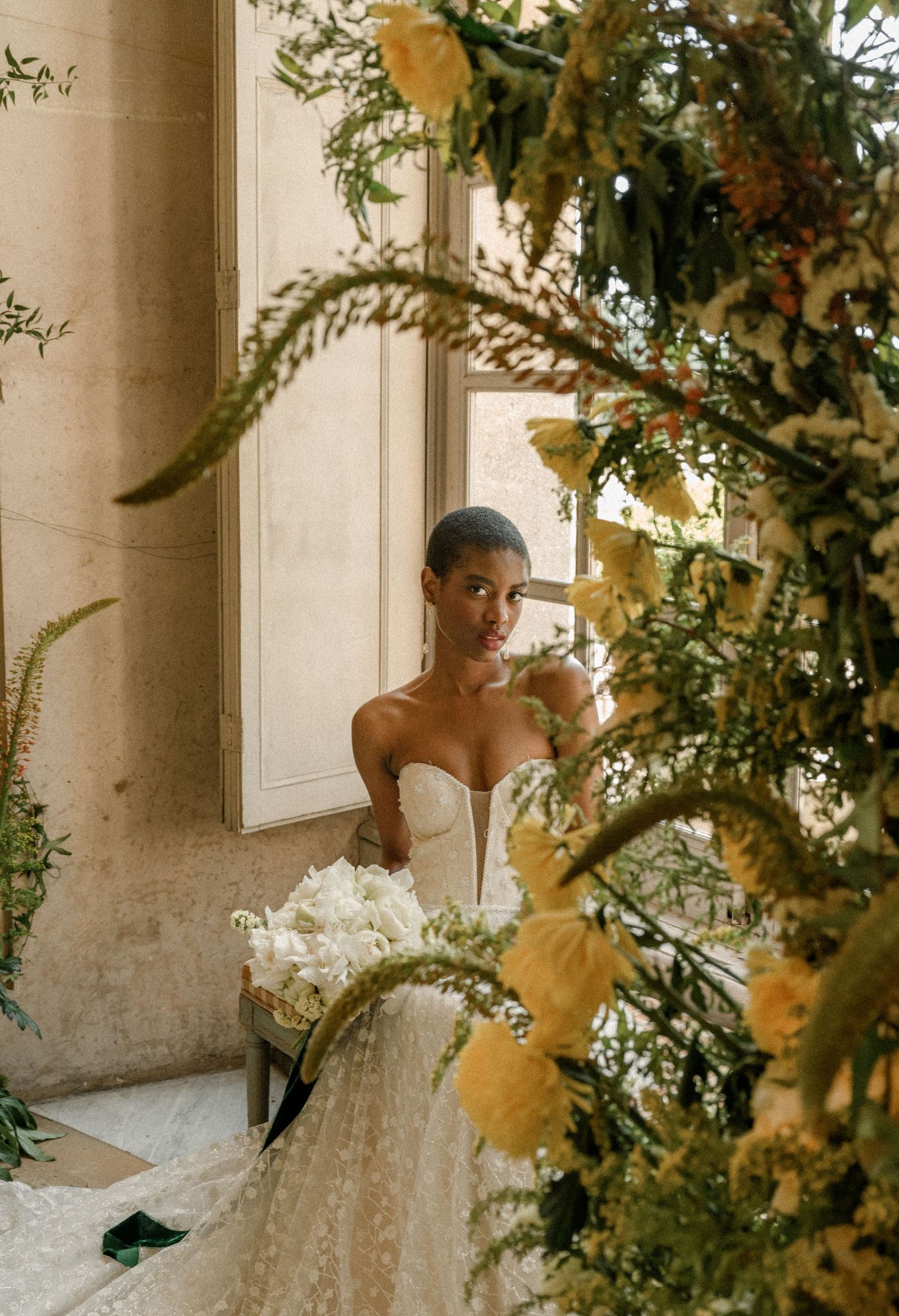 Wedding dress detail shot with floral arrangements framing elegant window setting.