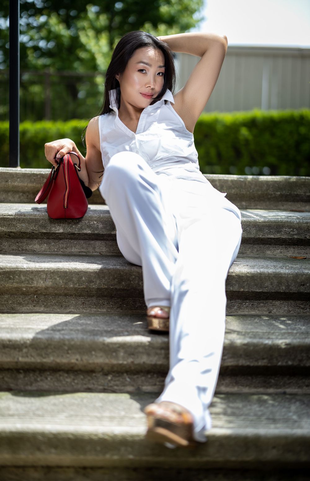 Relaxed outdoor pose on stone steps with white ensemble and red accessory.