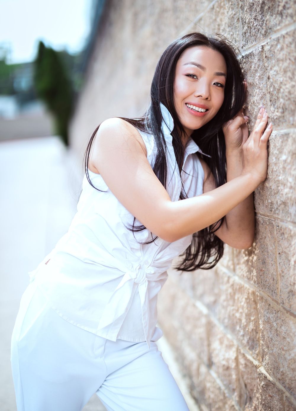 Elegant pose against stone wall wearing flowing white summer dress.
