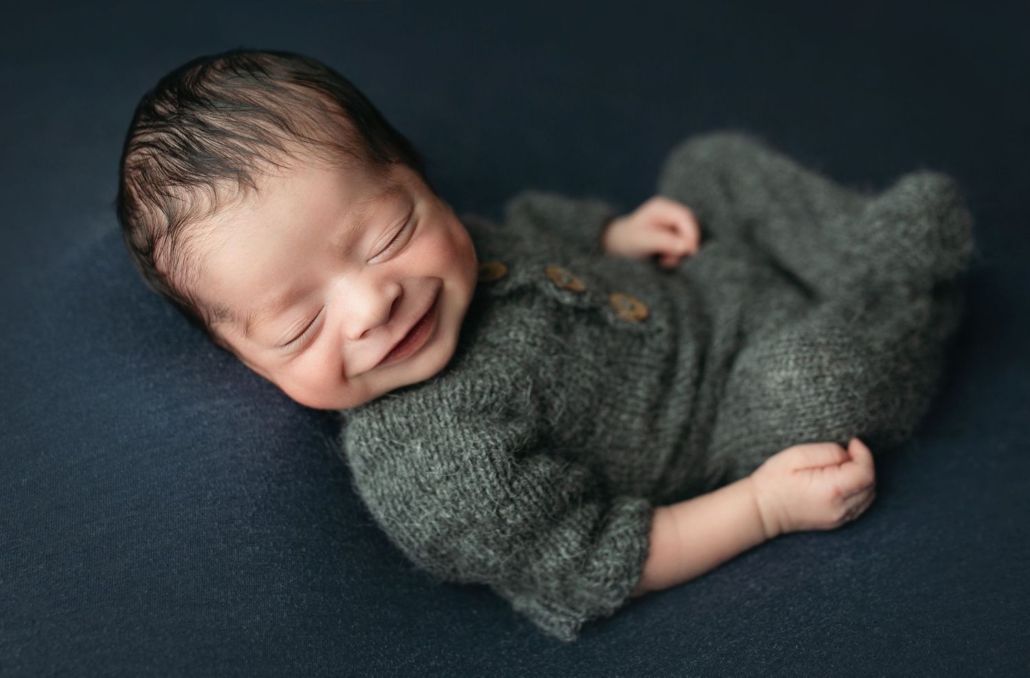 Hispanic newborn with a huge smile in a relaxed pose. Resting peacefully on a navy blue backdrop. - Easley SC newborn photographer