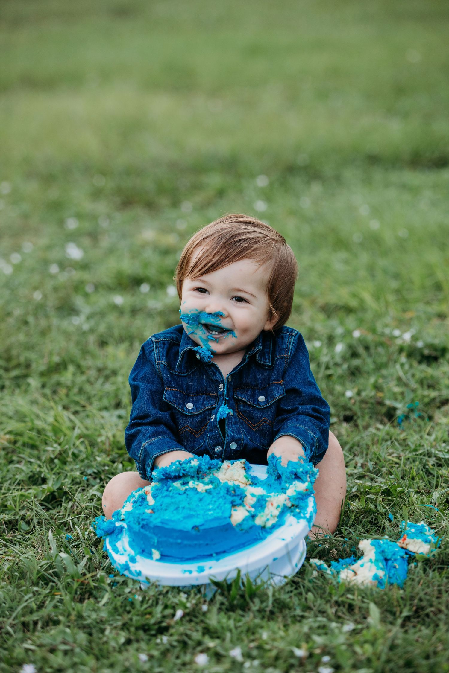 Smiling toddler with blue frosting on face enjoying cake smash photo session.