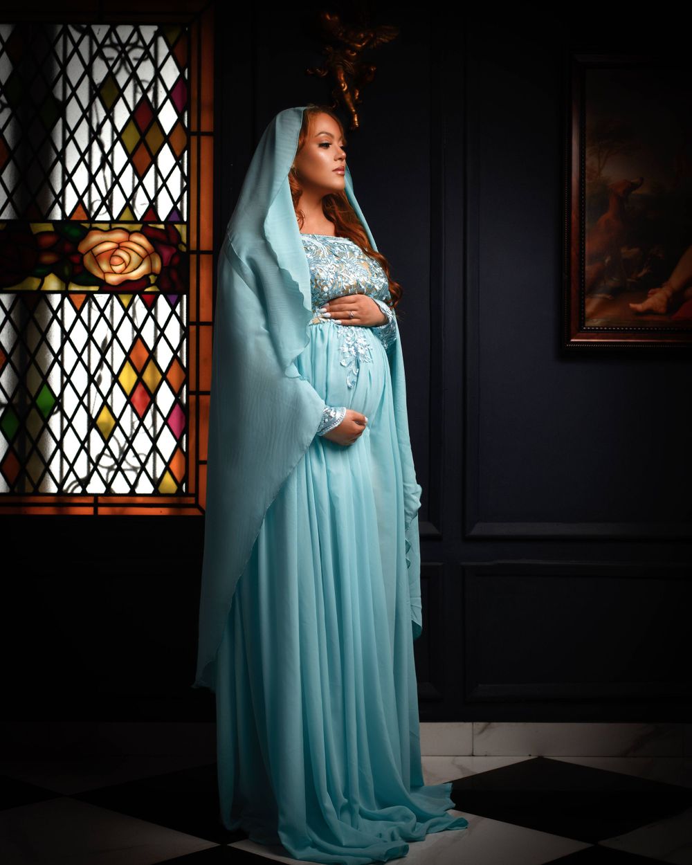 Maternity portrait in church setting with woman wearing flowing turquoise dress and veil.