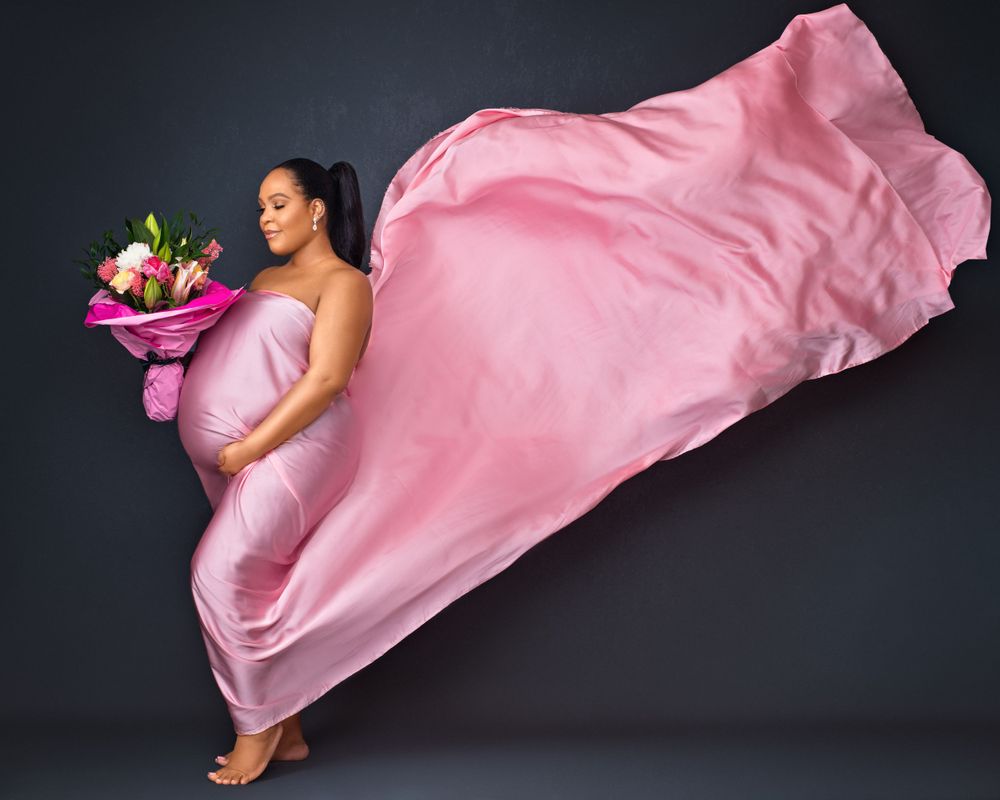 Creative fashion photo of a person in flowing pink silk fabric holding colorful flowers.