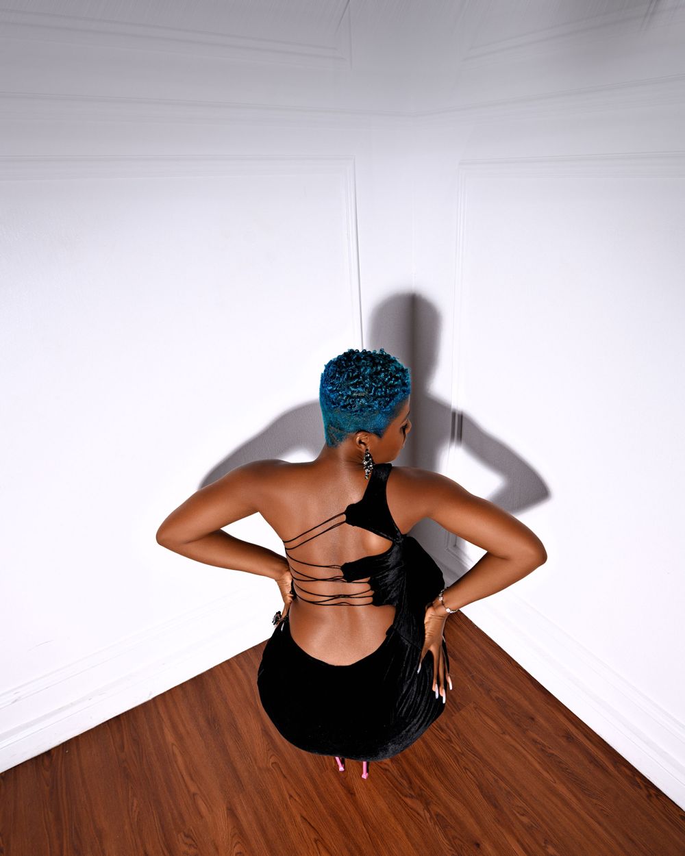 Artistic overhead view of figure in black outfit with blue hair against white background.