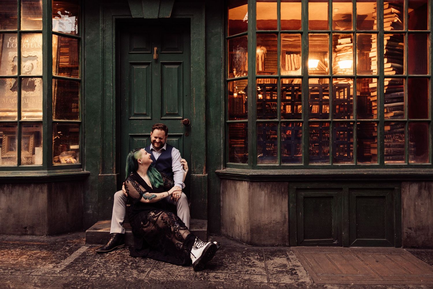 A couple poses intimately outside a vintage storefront with green doors and windows.