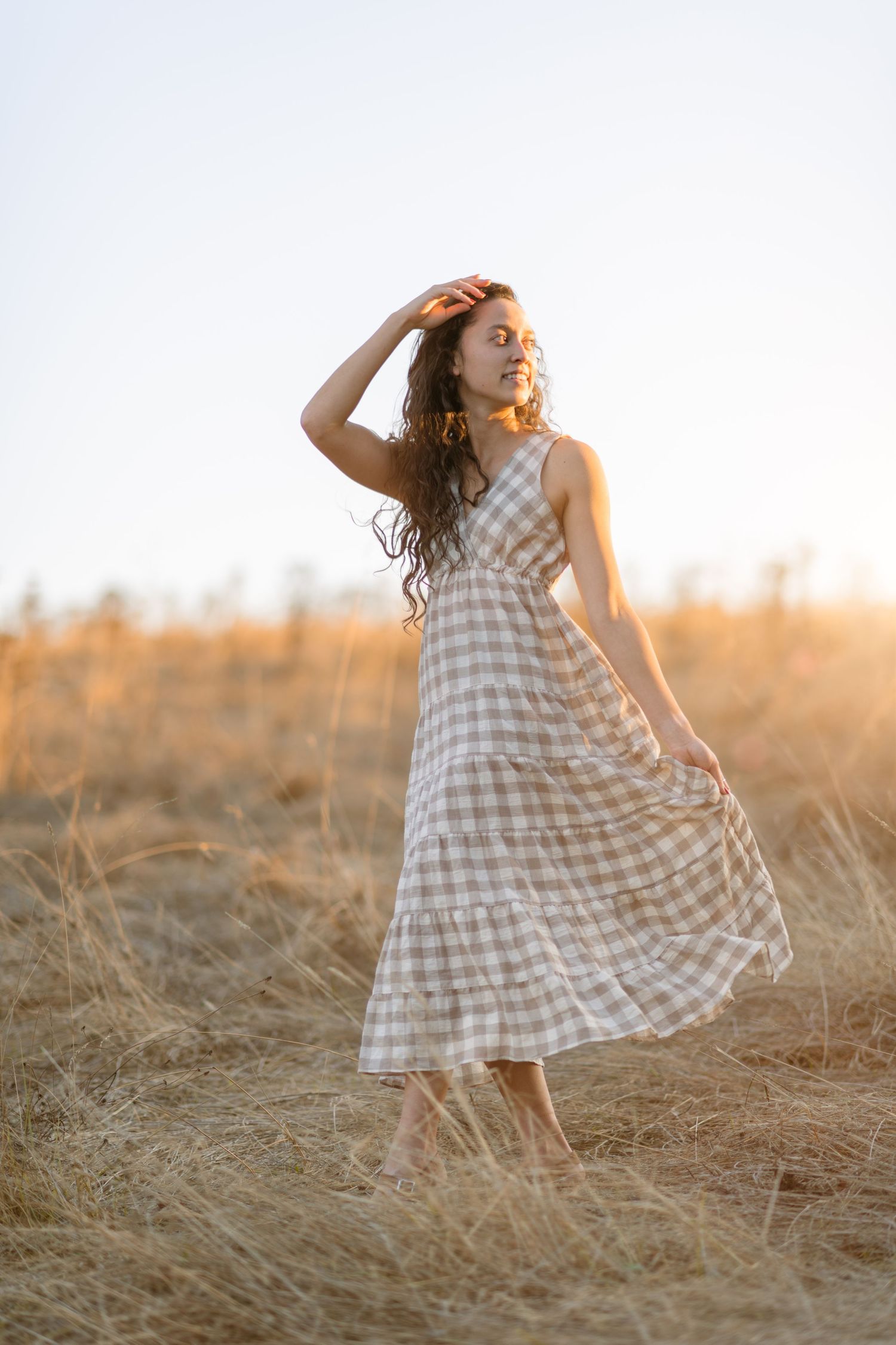 model wearing checkered sound dress walking and looking back at sun holding hair perfectly