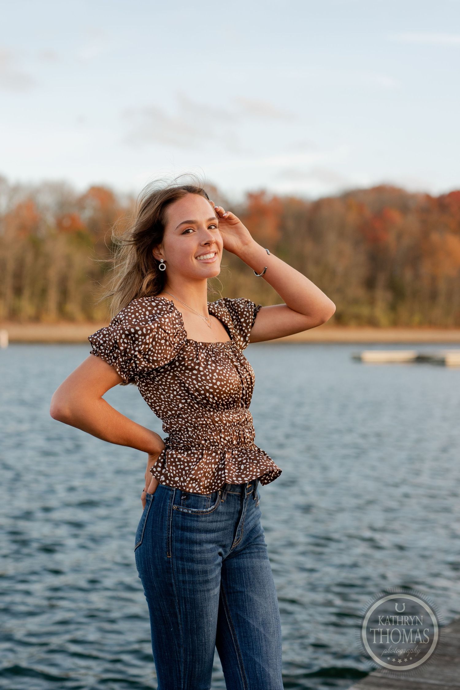 Autumn lakeside portrait with someone wearing a leopard print top and jeans on a wooden dock.