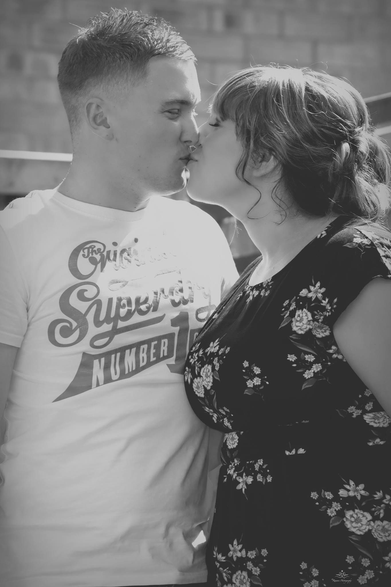A romantic black and white photo of a couple about to kiss, with one wearing a graphic t-shirt and the other in a floral dress.