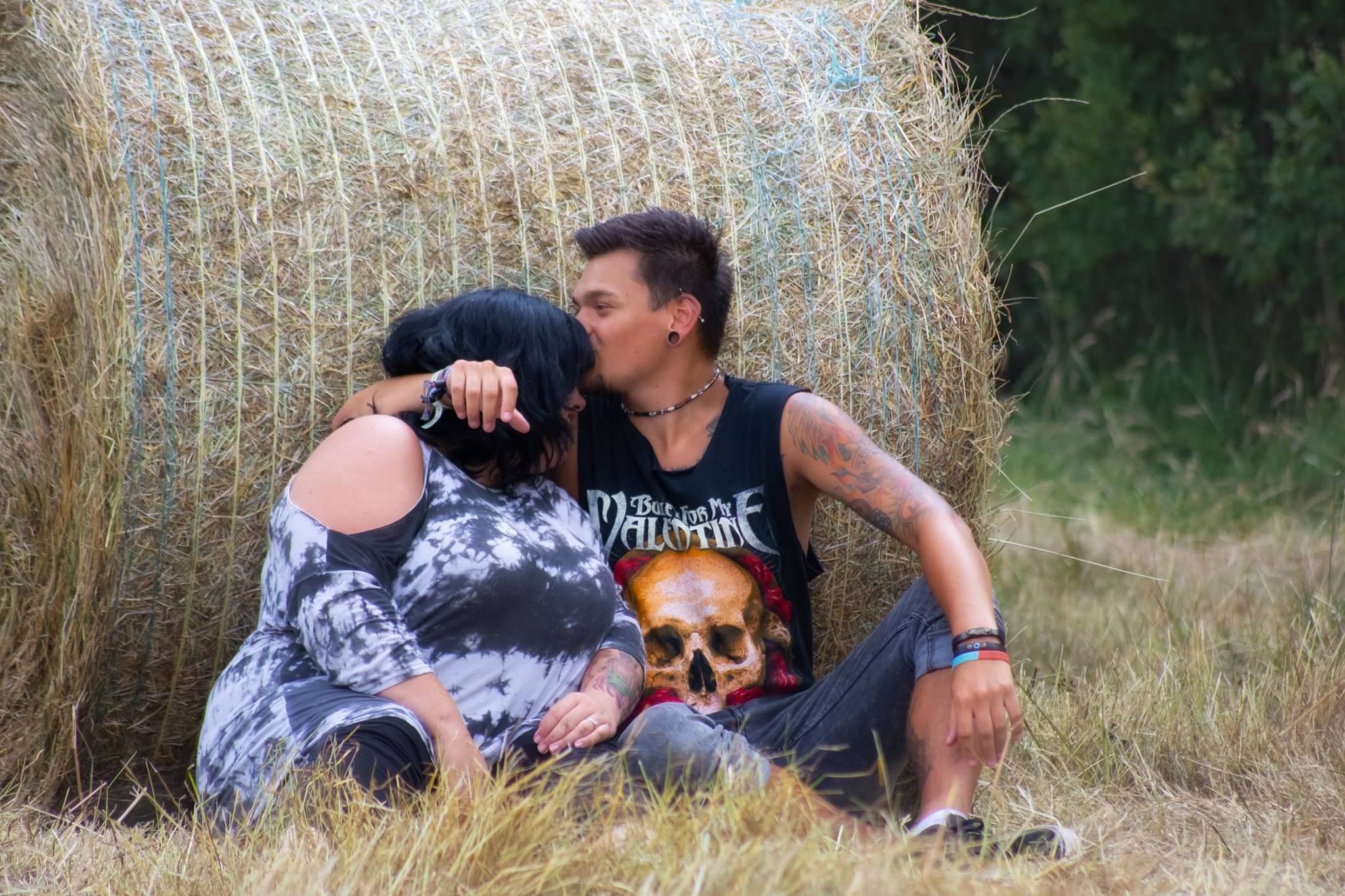 A couple sharing an affectionate moment while sitting by a hay bale in a field.