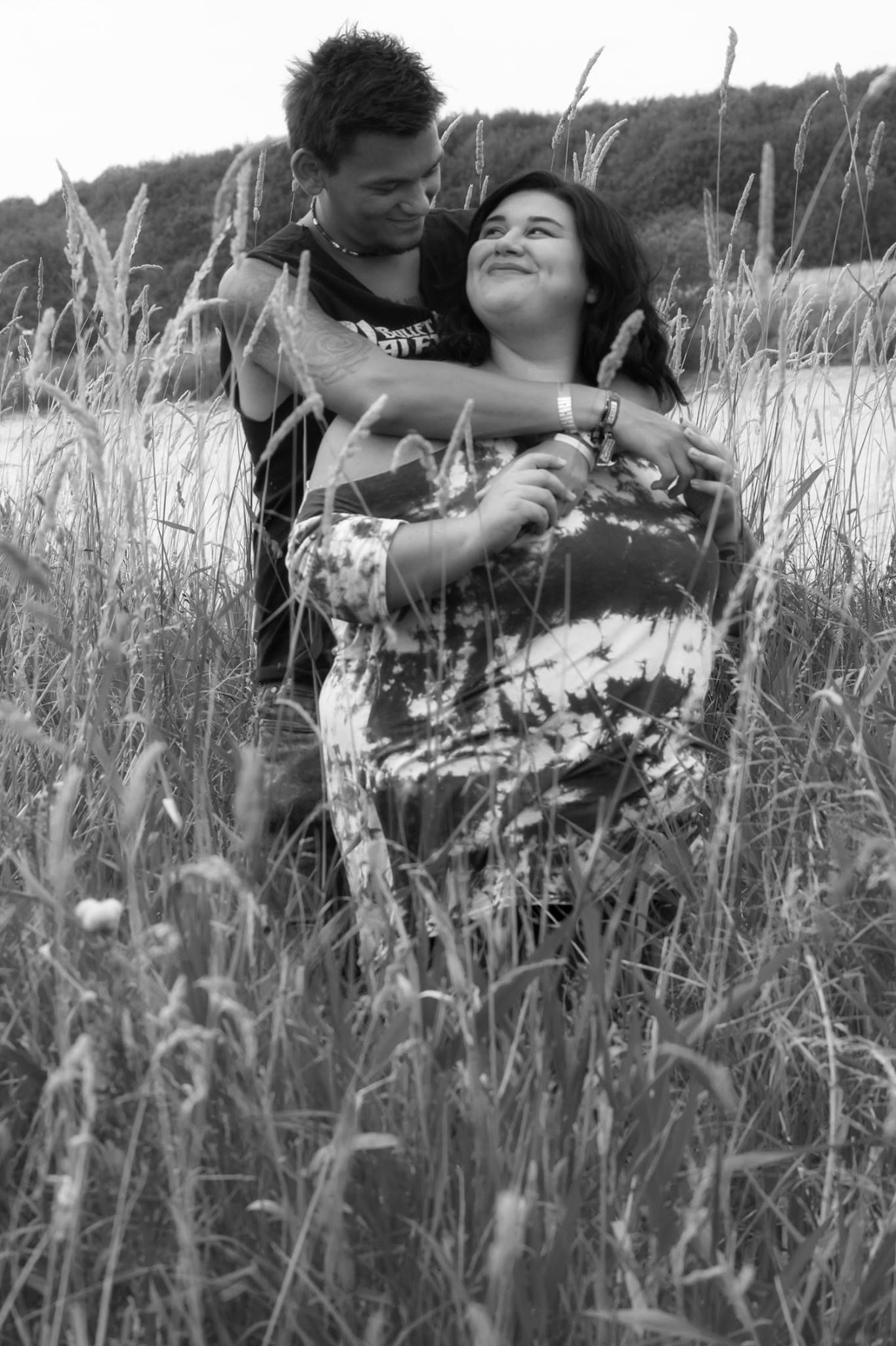 A tender black and white moment of a couple embracing in a field of tall grass.
