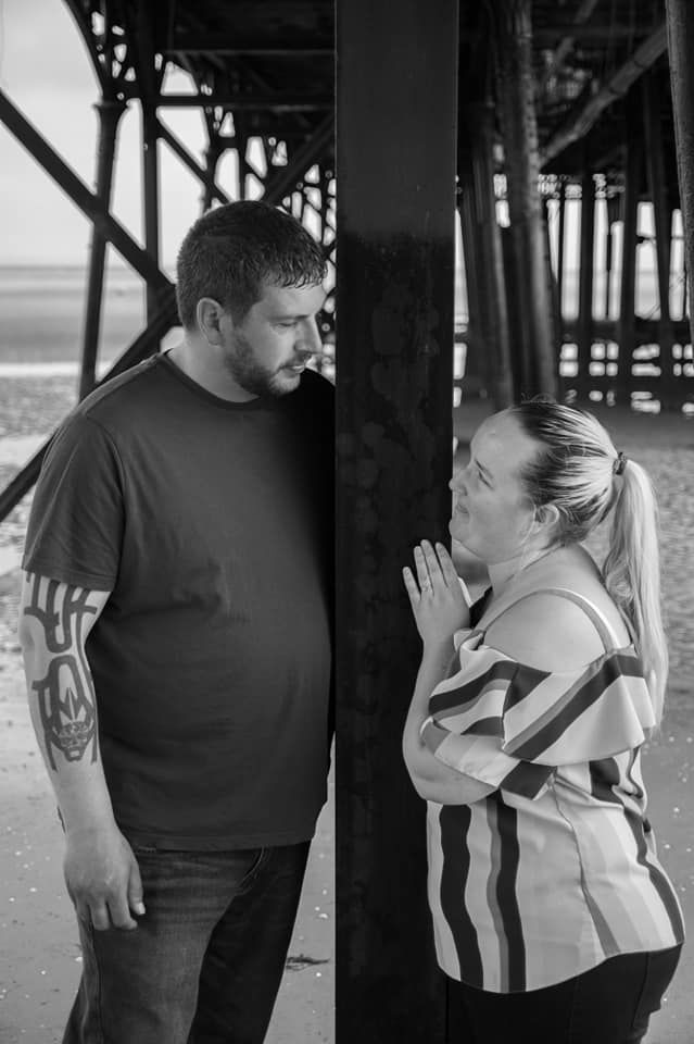 A black and white photo of a couple having an intimate moment under a pier.