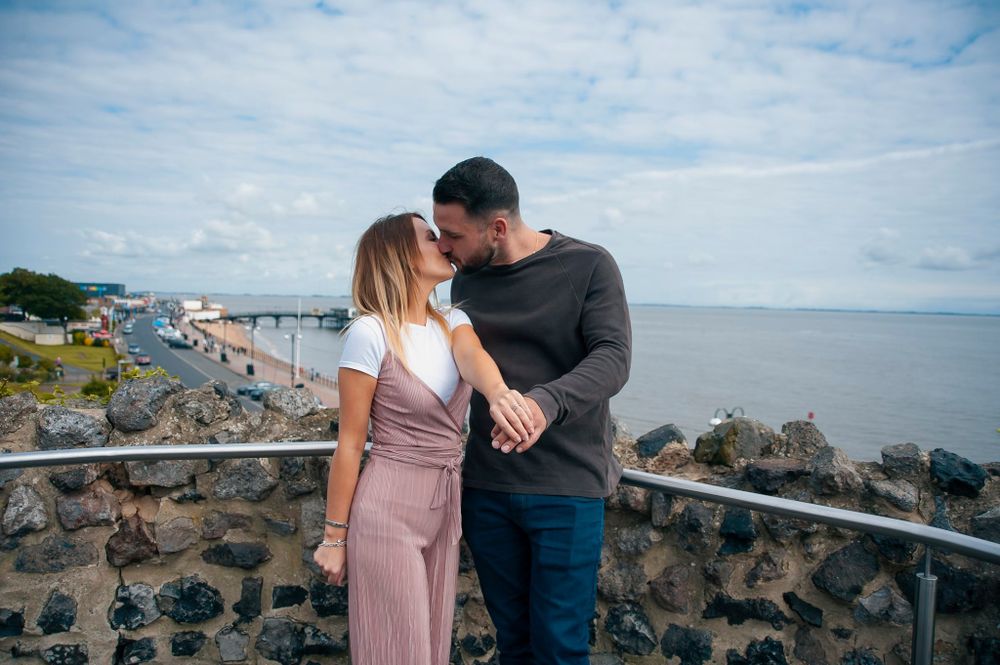 A couple sharing a tender moment overlooking a coastal view from a stone wall viewpoint.
