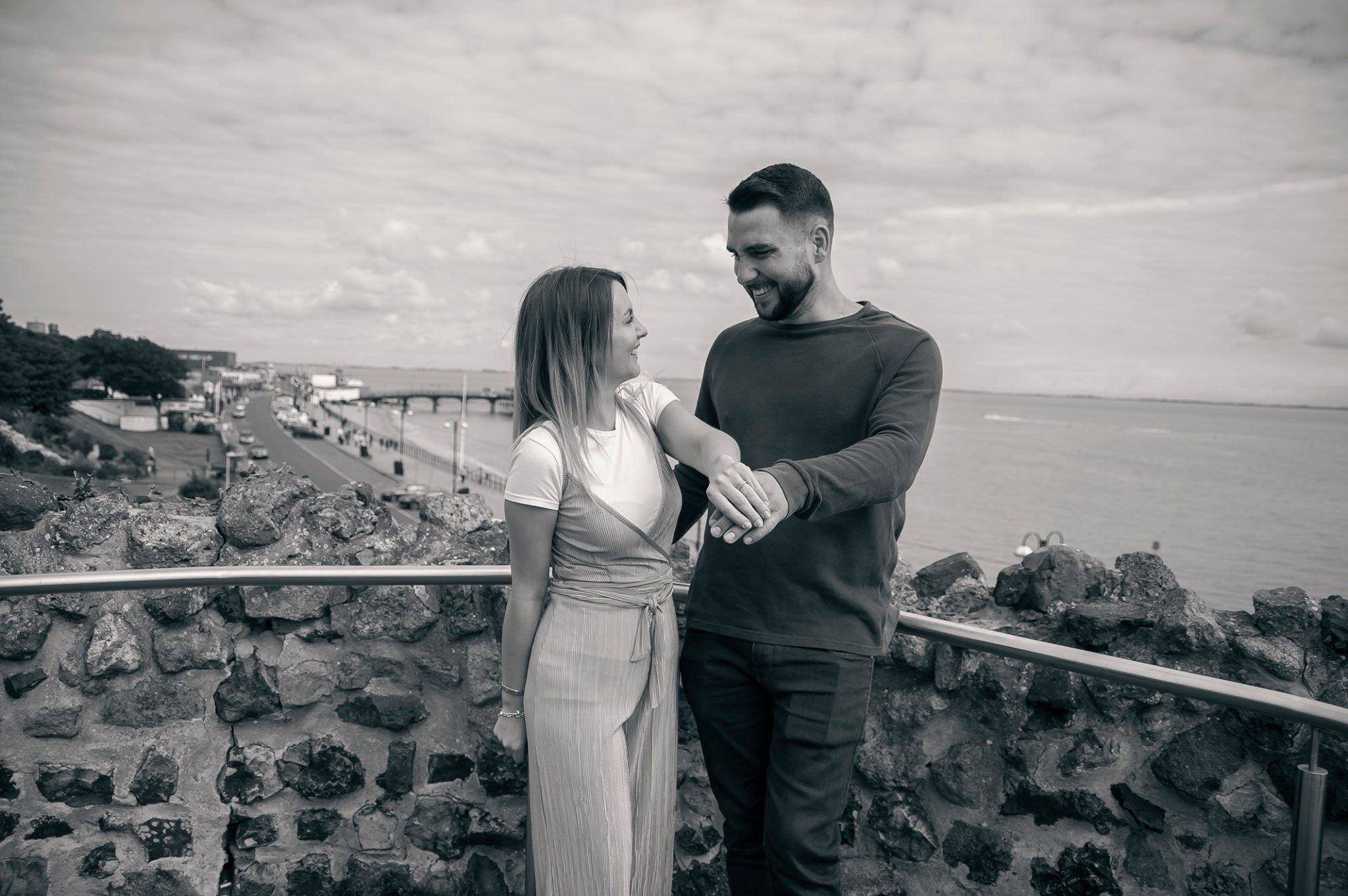 A couple in casual attire sharing an intimate moment against a seaside backdrop.