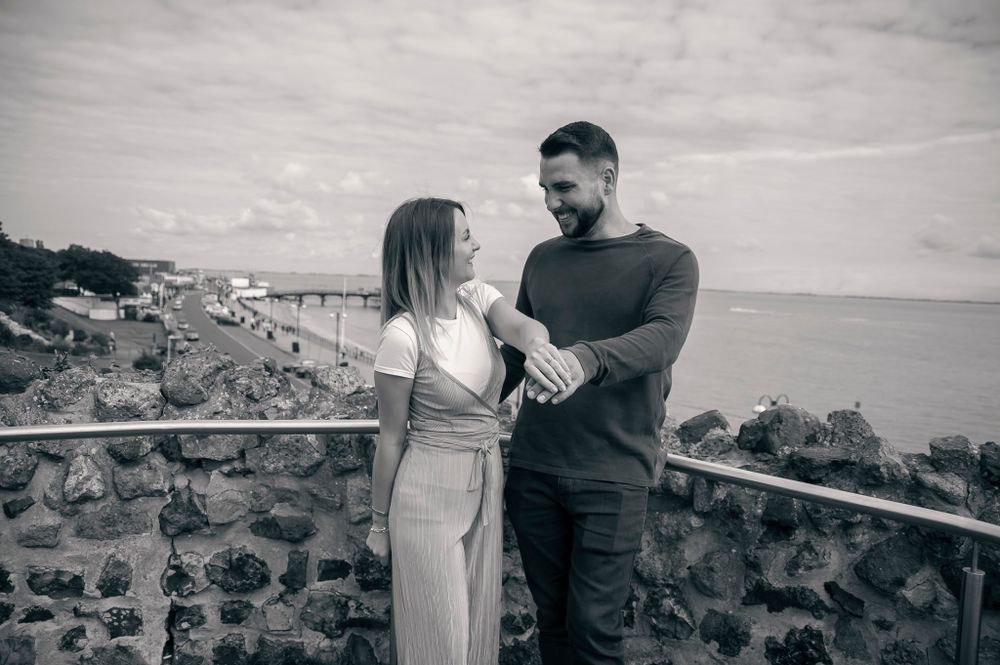 A couple in casual attire sharing an intimate moment against a seaside backdrop.