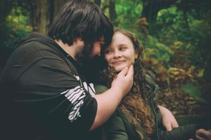 A tender romantic moment between a couple in a forest setting, with gentle natural lighting and foliage in background.