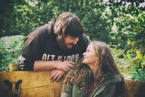 A playful romantic outdoor scene with a couple by a wooden log surrounded by greenery.
