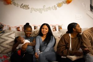 Friends gather on a couch under decorative banner with orange accents at a casual party.