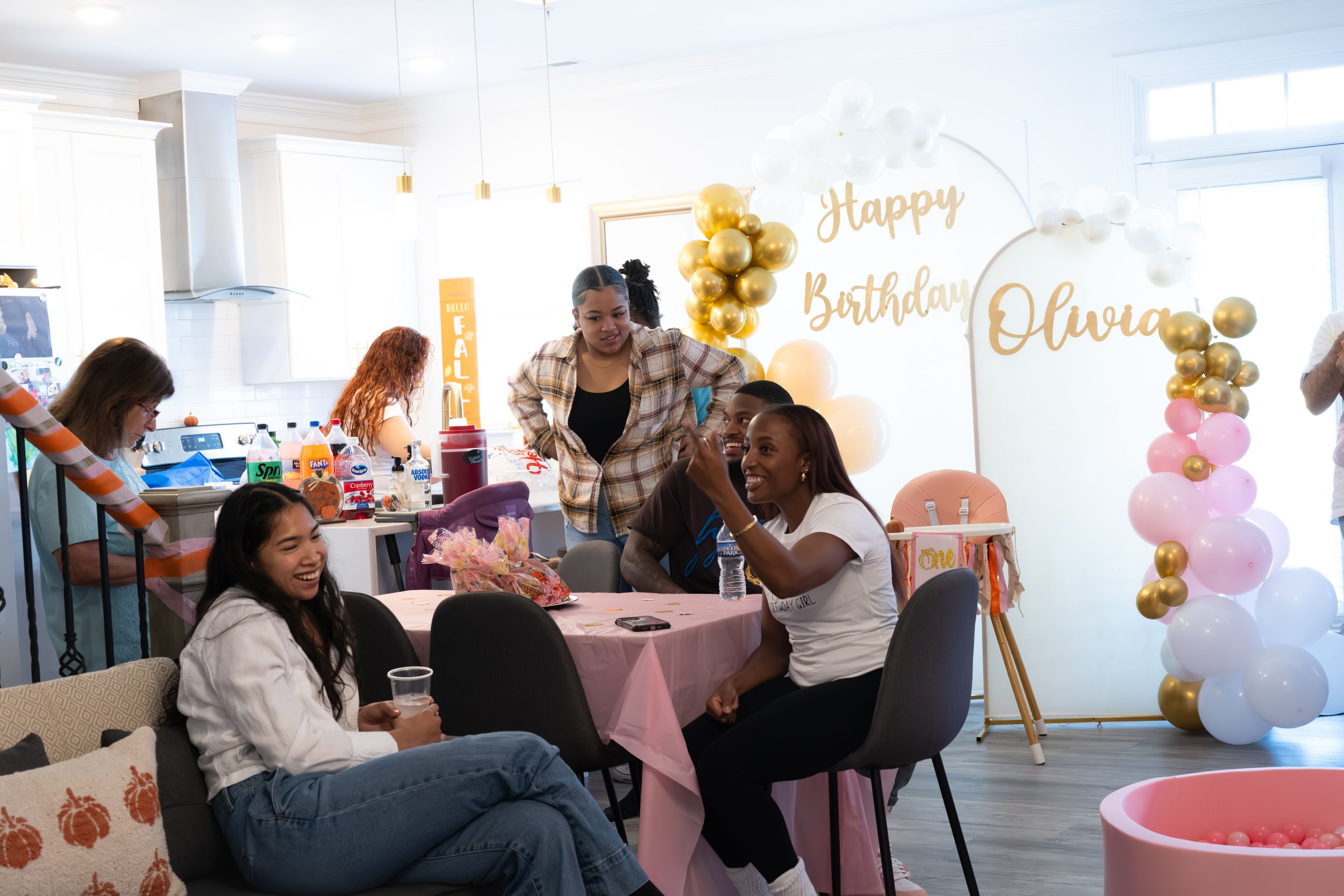 People gathered around pink-decorated tables at a birthday celebration with festive decorations and sunflowers.