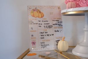Decorative pumpkin-themed party schedule displayed on white board with pink accents.