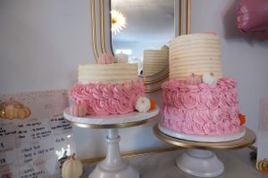 Three white and pink frosted cakes displayed on elegant white cake stands.