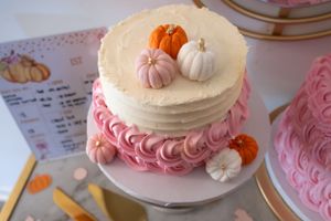 Close-up of tiered cake with pink frosting and miniature pumpkin decorations.