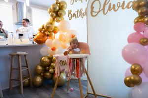 Party space decorated with gold and pink balloon garlands and celebratory signage.