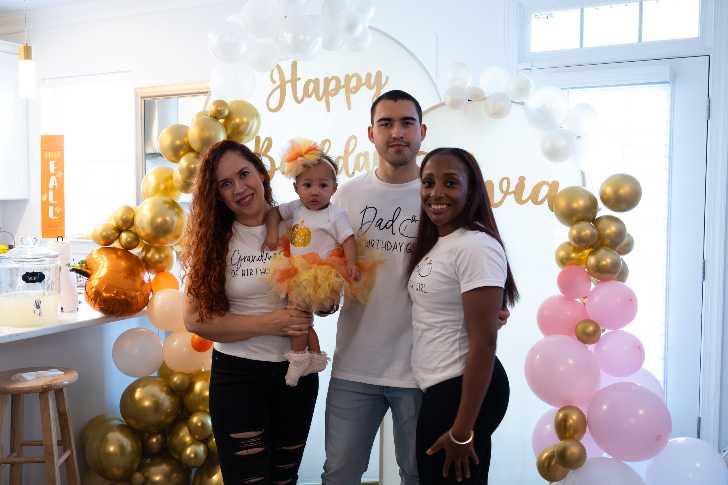 Celebratory gathering with gold and pink balloon arrangements and decorative banner.