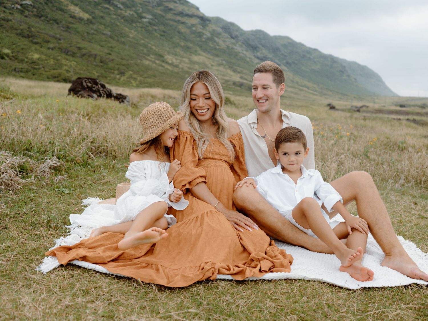 A beautiful family of four with an expecting mother and a mountain backdrop smiling on Oahu in Hawaii