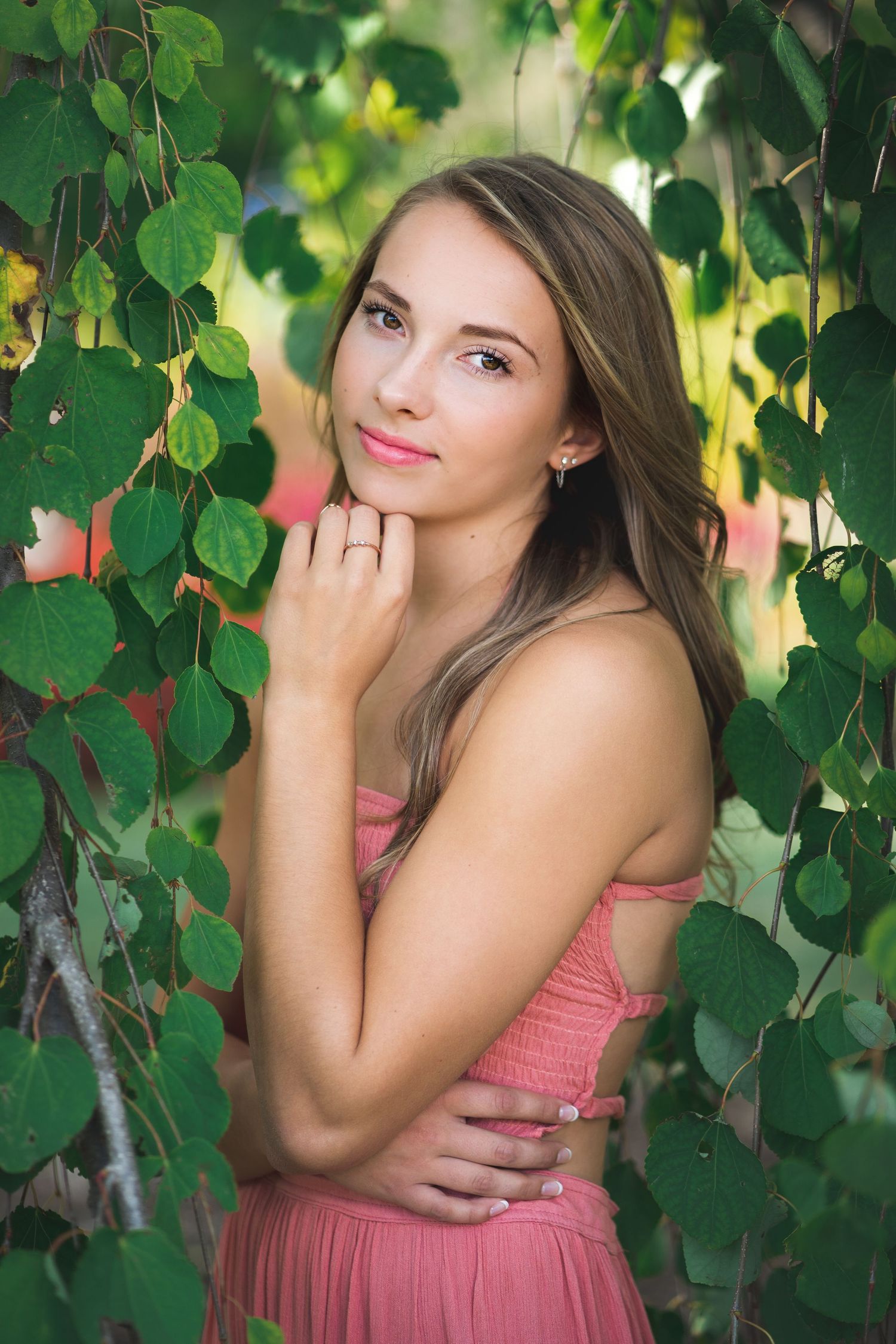 Portrait among green leaves wearing coral dress in natural lighting.