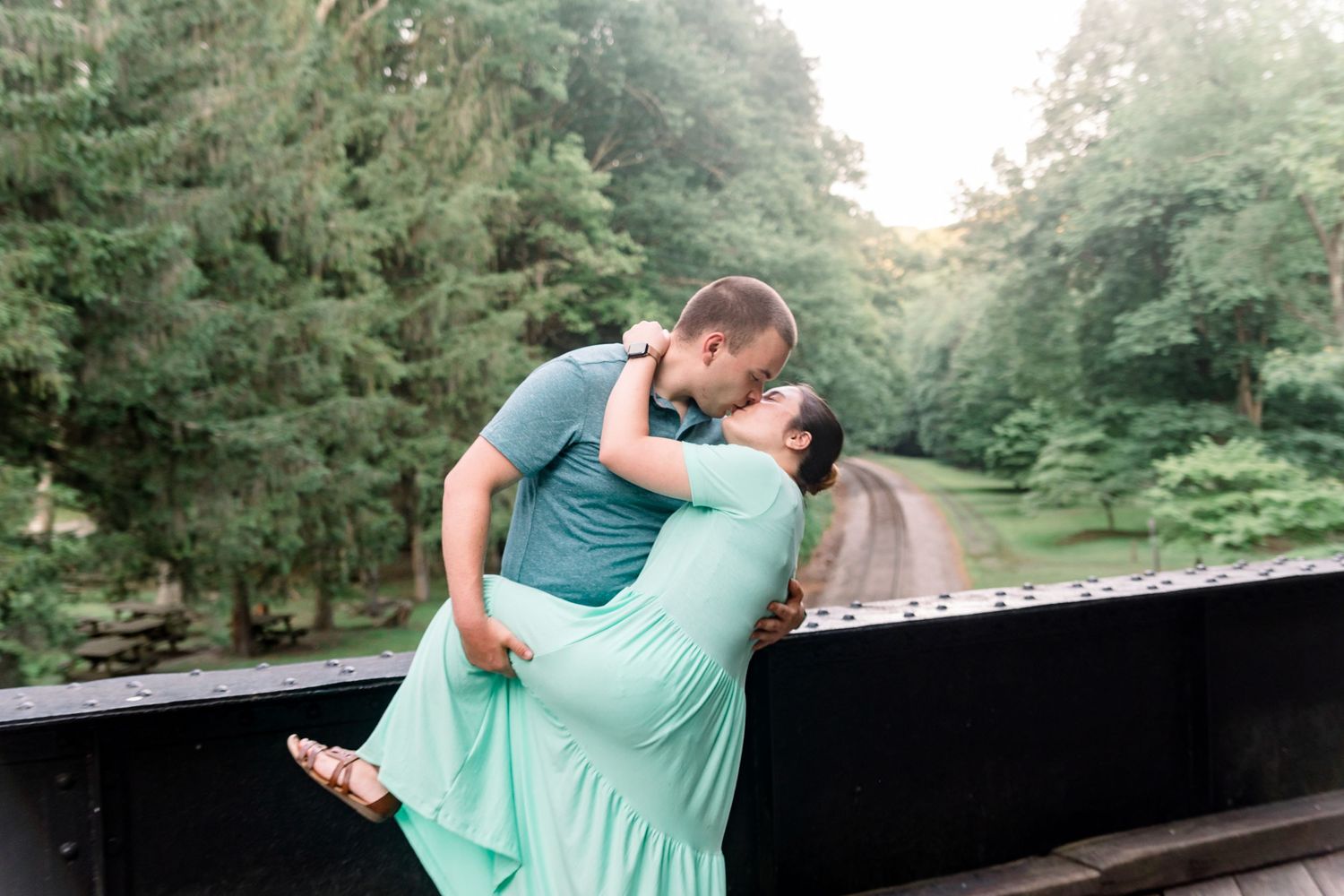 A romantic engagement photoshoot on a wooden bridge in a forest setting.