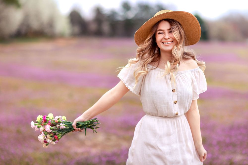 Woman in vintage dress and hat holding flowers in a blooming purple wildflower field.