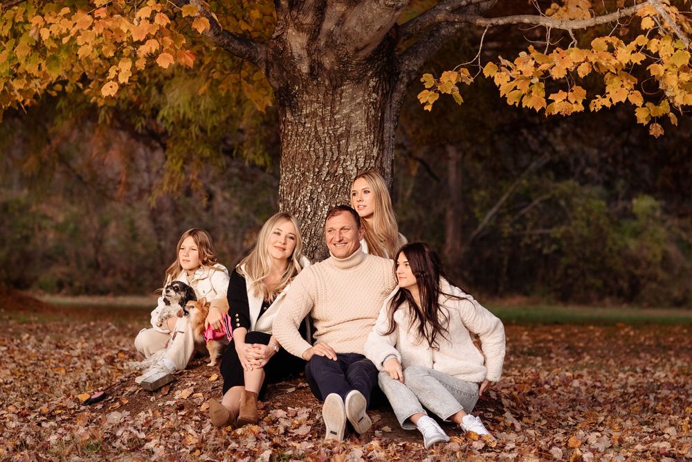Group in cream sweaters sits together under large autumn tree with golden leaves.