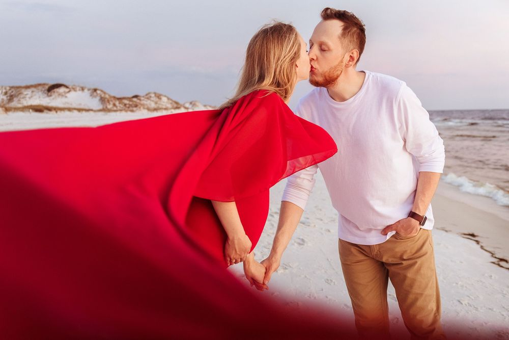A beach maternity session featuring a billowing red dress against the ocean backdrop.
