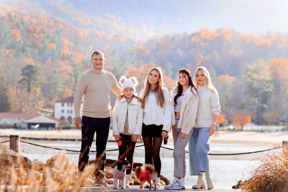 Group wearing coordinated cream and white outfits poses with small dog by lakeside during autumn.