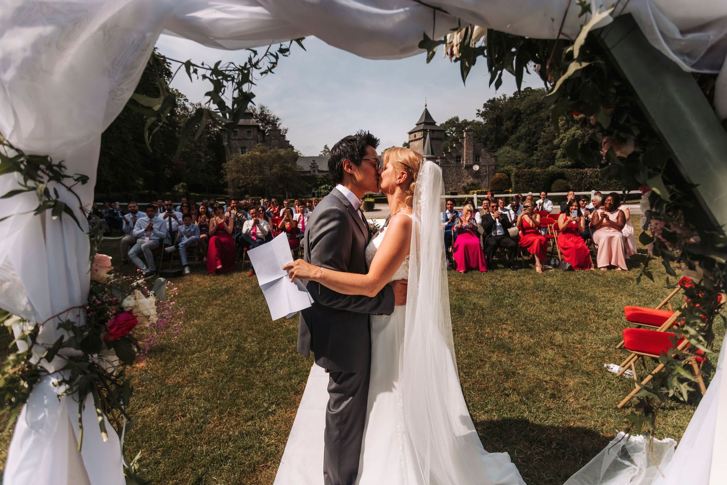 Wedding ceremony under white draped arch with guests seated on lawn watching couple's first dance.