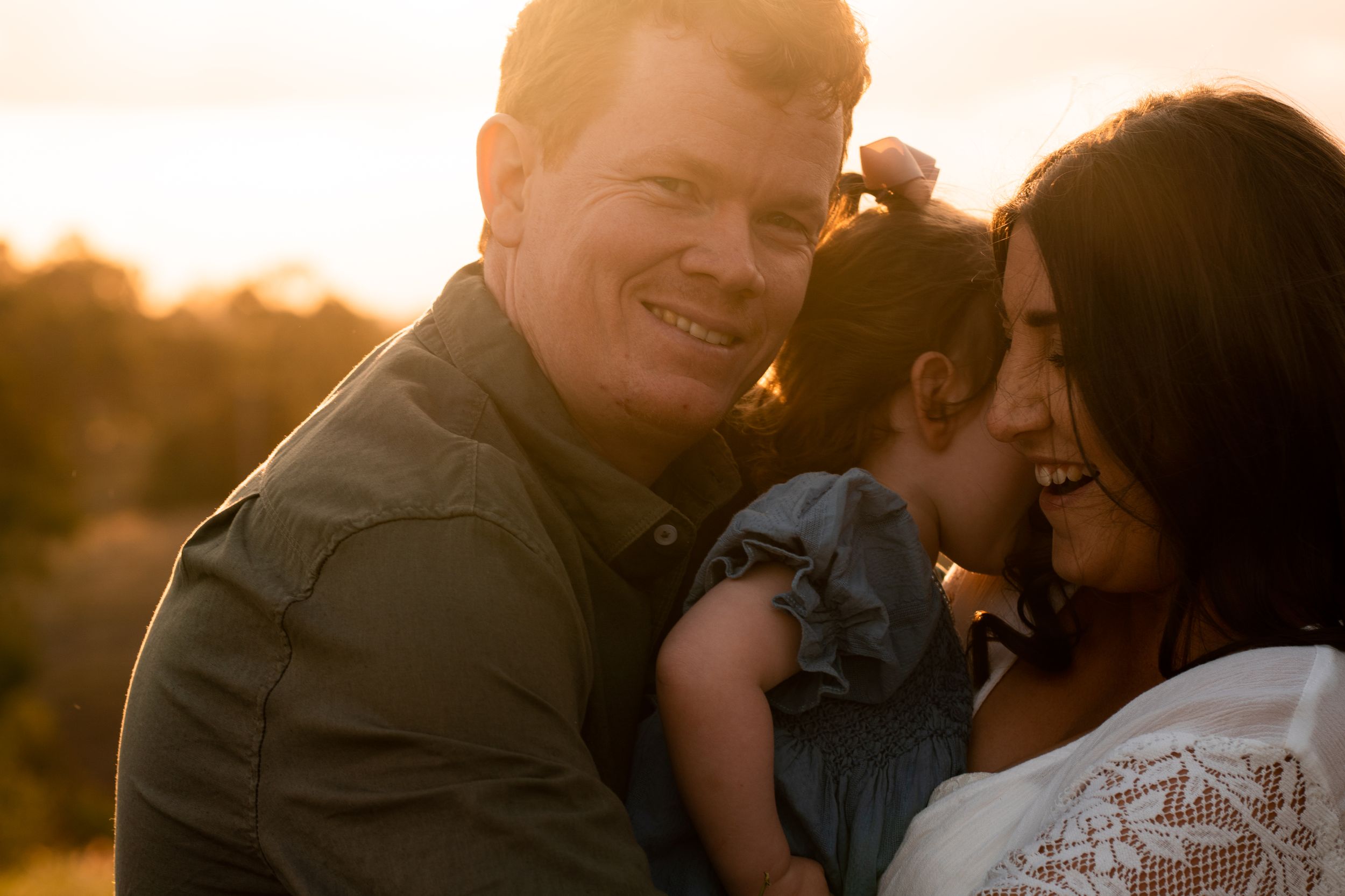 Close up of mother and father holding squirming toddler, while the three laugh together