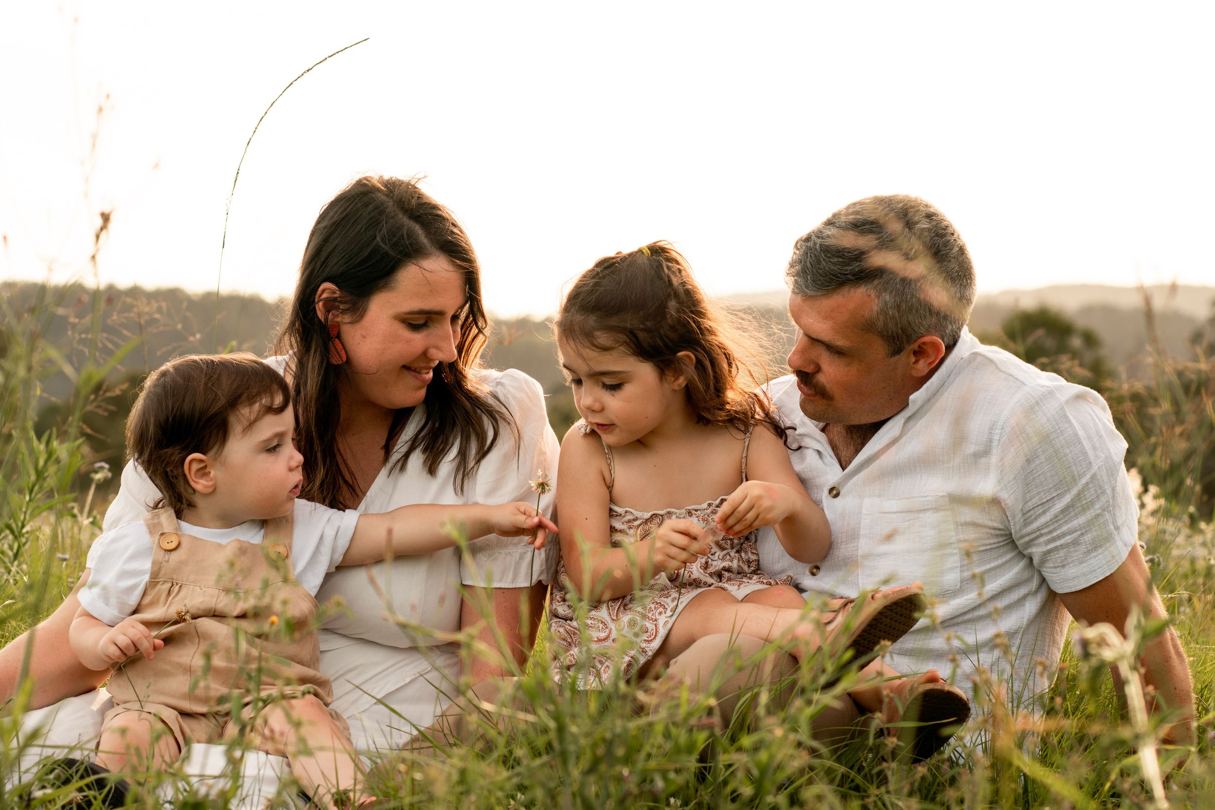 Young family seated amongst long grass at sunset, children on their parents' laps.