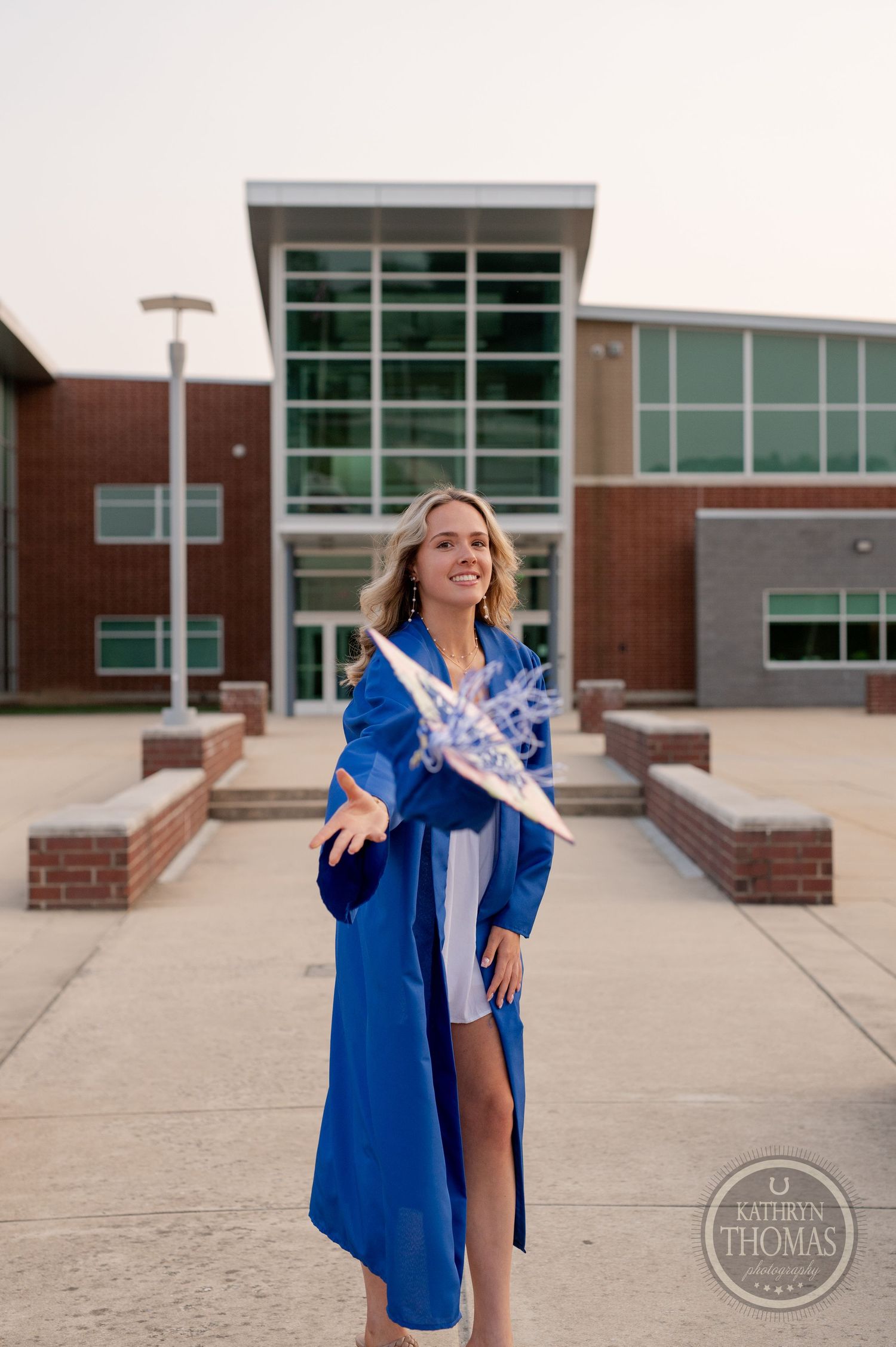 Graduate throws arms open joyfully while wearing blue graduation regalia.
