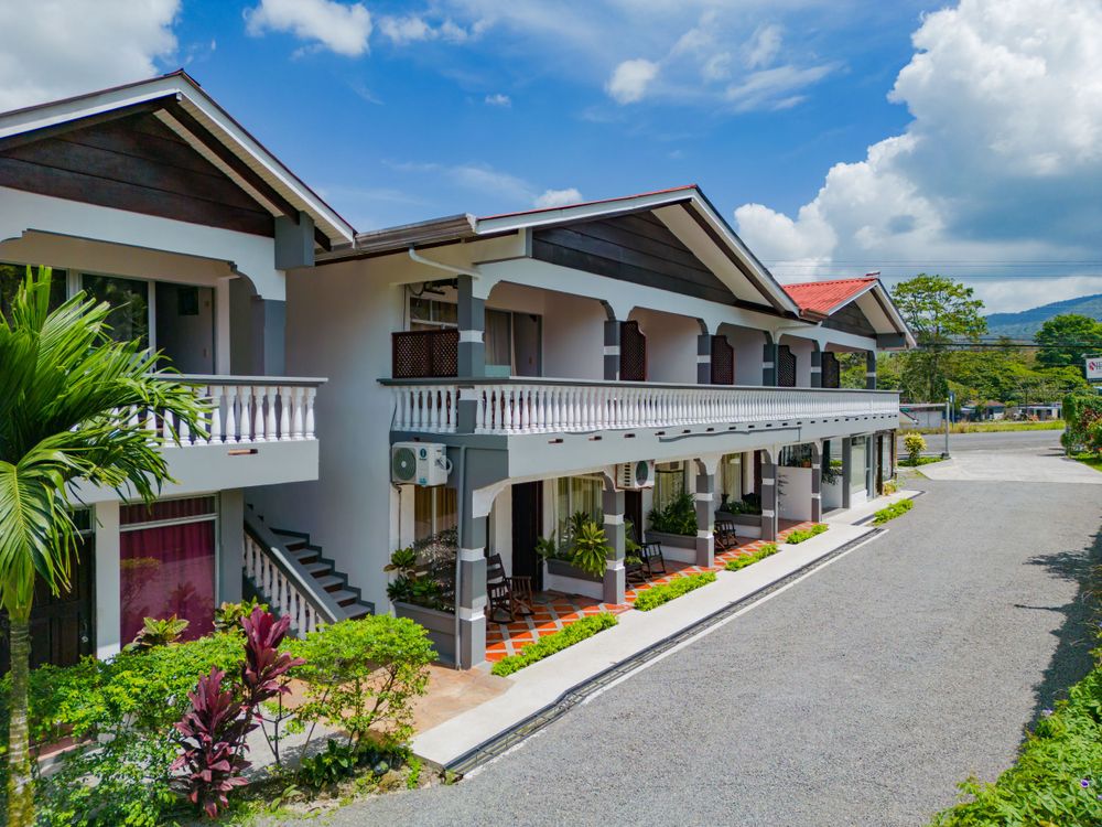 Modern two-story resort building with white balconies and tropical landscaping along a paved driveway.
