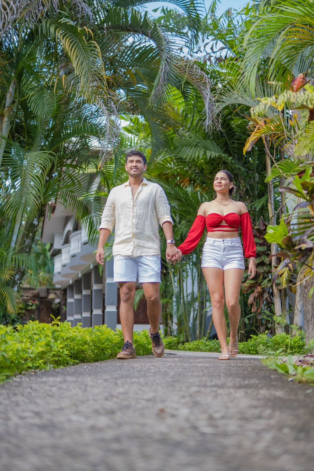 A couple strolling down a palm-lined pathway at a tropical resort.